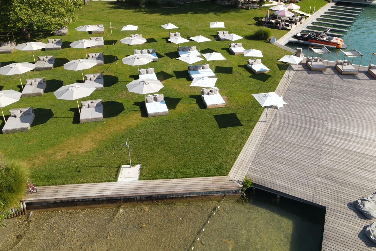 Luftaufnahme der Liegewiese mit Daybeds, Steganlage und Bootsanlegestelle am Wörthersee